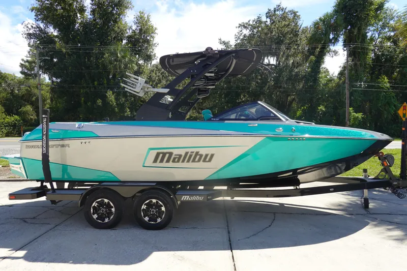 Slide: The Image of 2019 Malibu Wakesetter 23 LSV boat on trailer, teal and white design, parked outdoors. - 4
