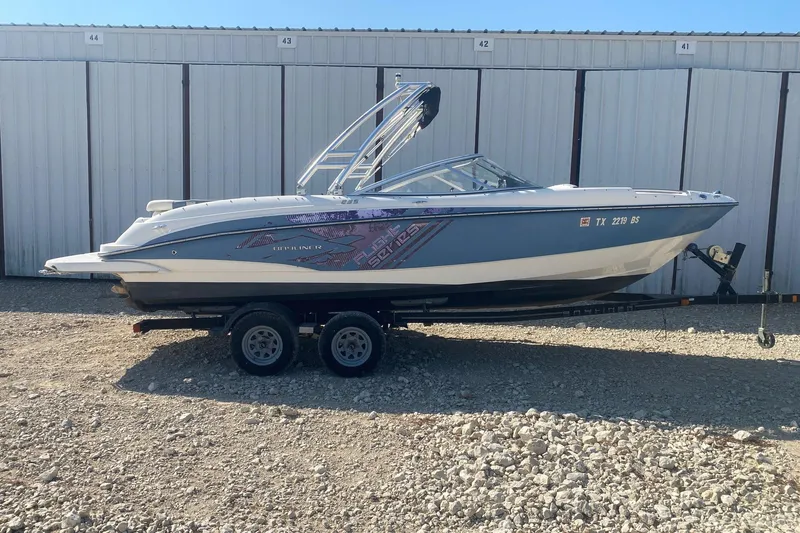 The Image of 2012 Bayliner 235 Bowrider boat on trailer, parked in front of storage units. - 0