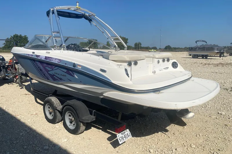 Slide: The Image of 2012 Bayliner 235 Bowrider on trailer, parked on gravel, under clear blue sky. - 2