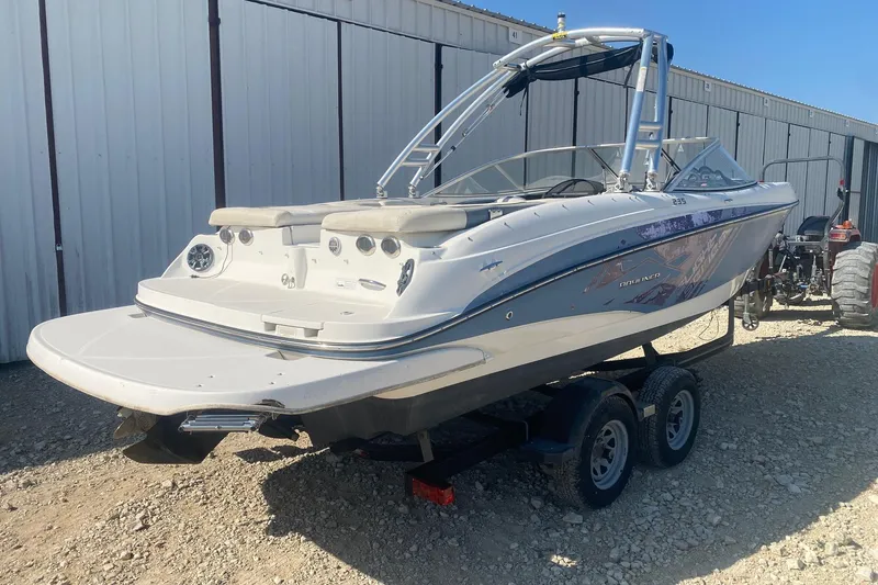 Slide: The Image of 2012 Bayliner 235 Bowrider boat on trailer, parked outdoors near a metal building. - 4
