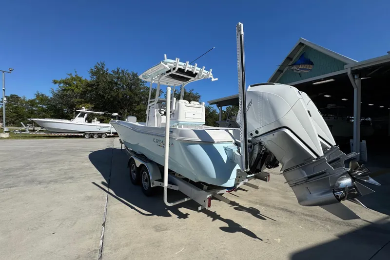 Slide: The Image of 2026 Caymas 281 HB boat with powerful outboard motor on trailer, parked near a boathouse. - 19