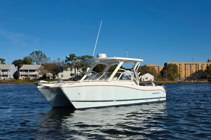 Slide: The Image of 2022 World Cat 255 DC boat on calm water, with buildings in the background. - 2