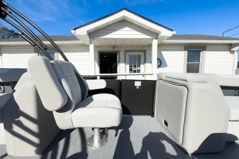 Slide: The Image of 2026 Godfrey Sweetwater 22' Tritoon interior with split bench seating, docked near a white building. - 43