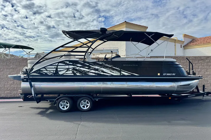 The Image of 2015 Bennington 2575 QCW pontoon boat on trailer, parked outdoors under cloudy sky. - 0