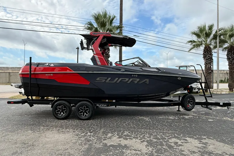 The Image of 2026 Supra SE 550 boat on trailer, black and red design, parked outdoors. - 1