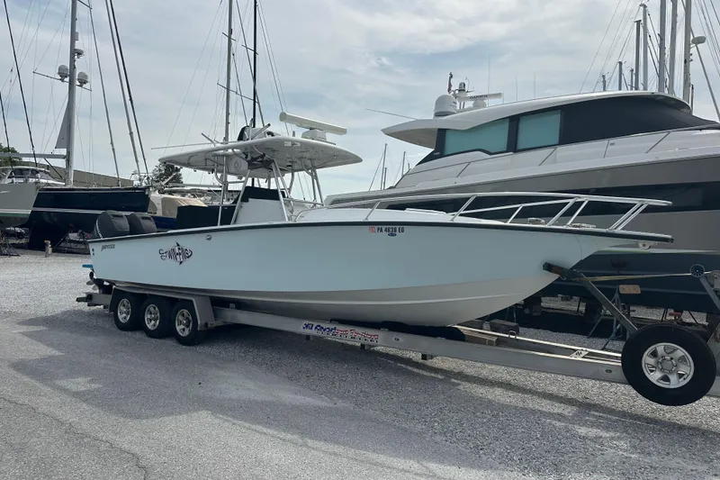The Image of 1999 Jupiter 31 Cuddy boat on trailer, parked in marina with other yachts. - 0