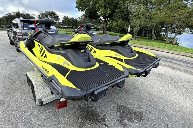 Slide: The Image of Two 2023 Yamaha WaveRunner VX110 jet skis on a trailer, parked near a lake. - 2