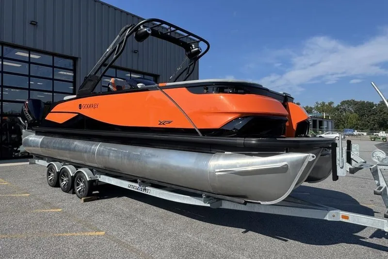 The Image of 2026 Godfrey XP 2700 TWIN pontoon boat on trailer, vibrant orange design, parked outdoors. - 0