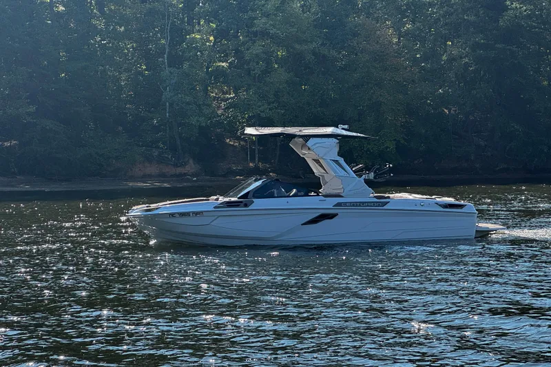 Slide: The Image of 2025 Centurion Ri245 boat cruising on a sunlit lake with forested background. - 2