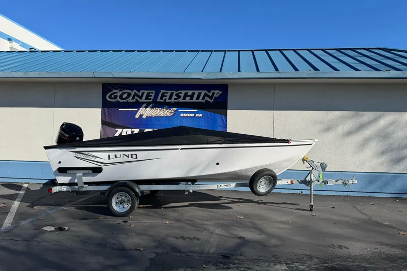 The Image of 2026 Lund 1650 Angler SS boat on trailer, parked outside a building. - 0