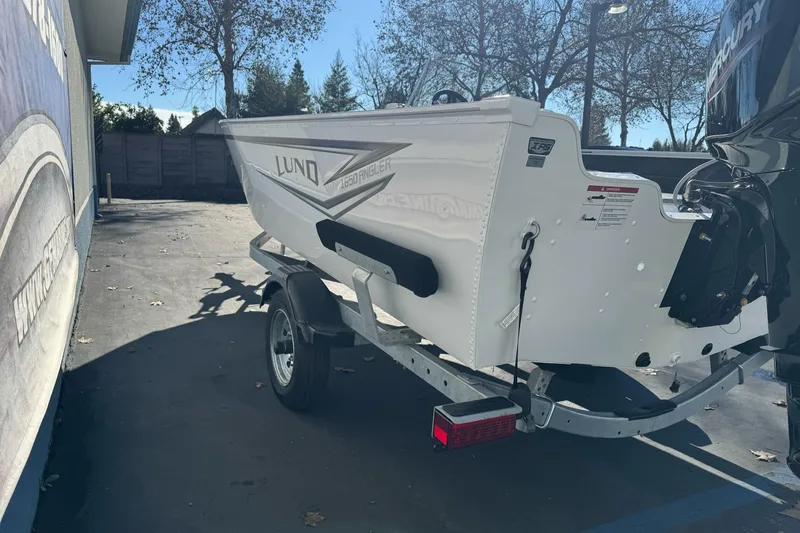 Slide: The Image of 2026 Lund 1650 Angler SS boat on trailer, parked outdoors in sunny setting. - 5