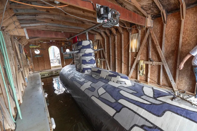 Slide: The Image of 2023 Submarine 28 Composite Construction in a wooden boathouse, featuring a camouflage design. - 10