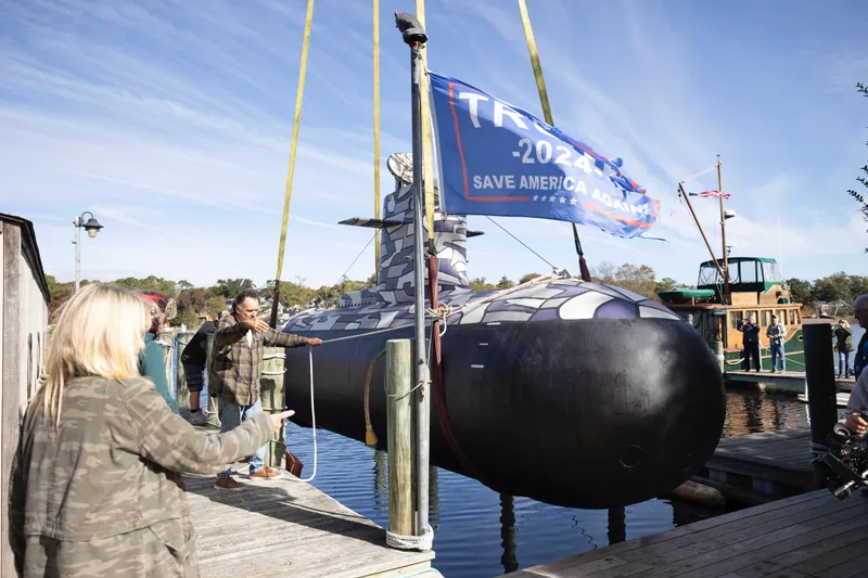 Slide: The Image of 2023 Submarine 28 Composite Construction with political banner at dockside event. - 12