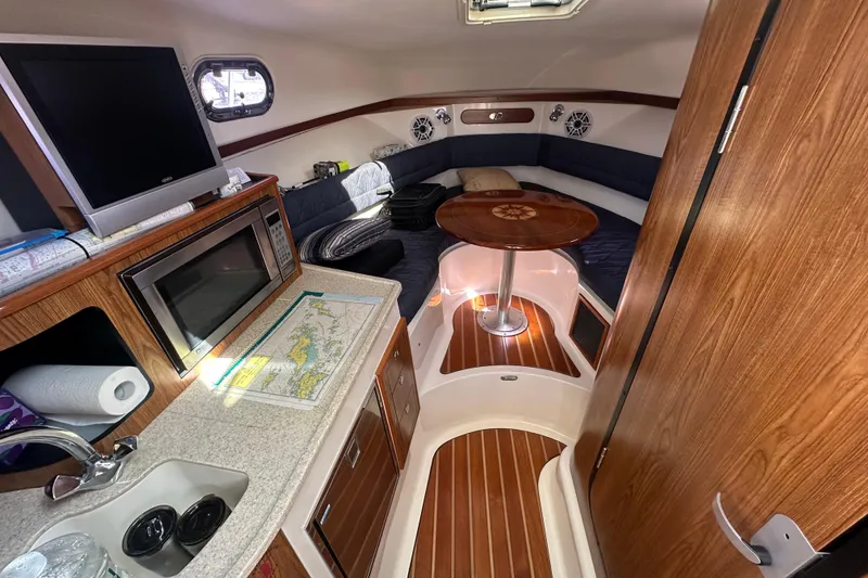 Slide: The Image of 2010 Pursuit OS 315 Offshore cabin interior with kitchenette, seating, and wooden accents. - 12