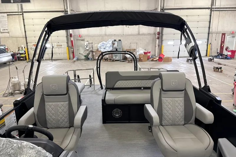 Slide: The Image of 2026 Godfrey Sweetwater 22' Tritoon interior with plush seating in a spacious warehouse. - 12