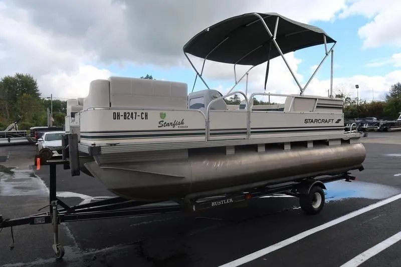 Slide: The Image of 1999 Starcraft Starfish 180 pontoon boat on trailer, parked outdoors under cloudy sky. - 11