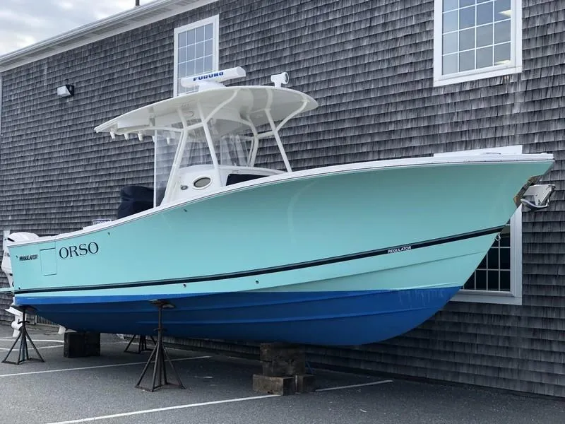 Slide: The Image of 2018 Regulator 31 boat in light blue, docked near a shingled building. - 4
