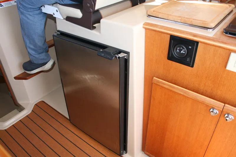 Slide: The Image of Interior of 2018 Ranger Tugs R-23 showing a compact fridge and wooden cabinetry. - 13