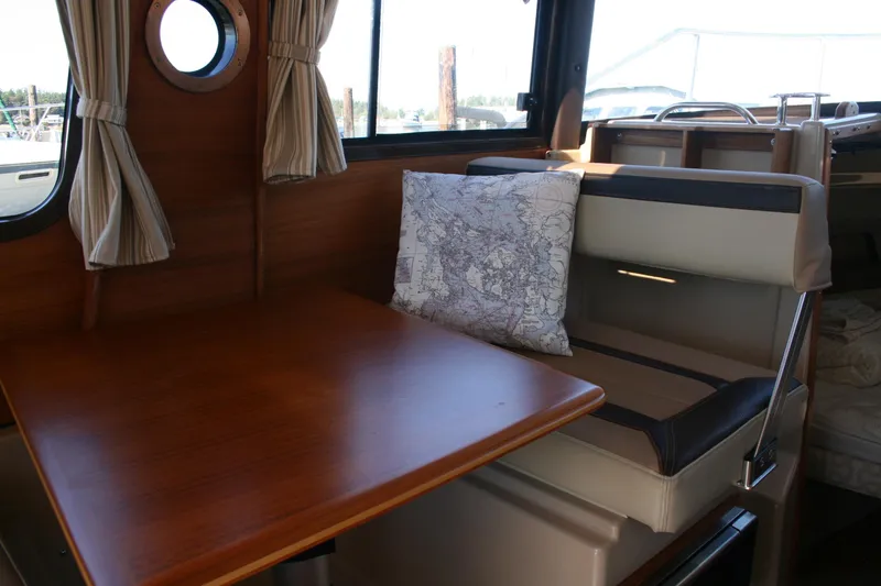 Slide: The Image of 2018 Ranger Tugs R-23 interior with wooden table, map-themed pillow, and porthole window. - 17