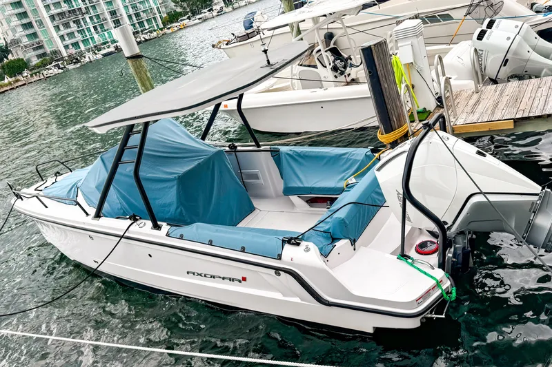 Slide: The Image of 2024 Axopar 25 Cross Top boat docked in marina, featuring sleek design and blue covers. - 1