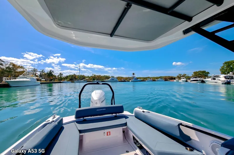 Slide: The Image of 2024 Axopar 25 Cross Top boat on serene blue water, surrounded by yachts. - 2