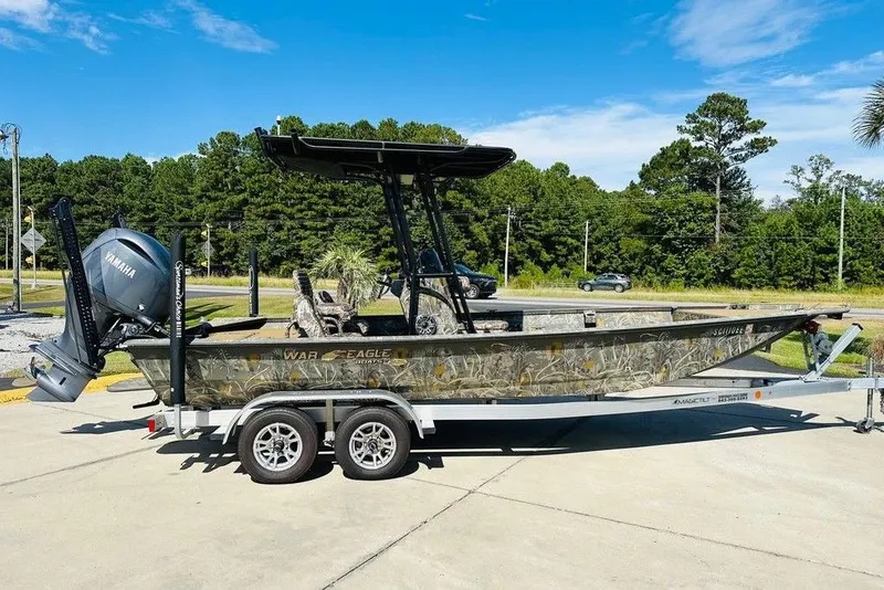 Slide: The Image of 2024 War Eagle 2170 Blackhawk boat on trailer, camo design, Yamaha motor, outdoor setting. - 0