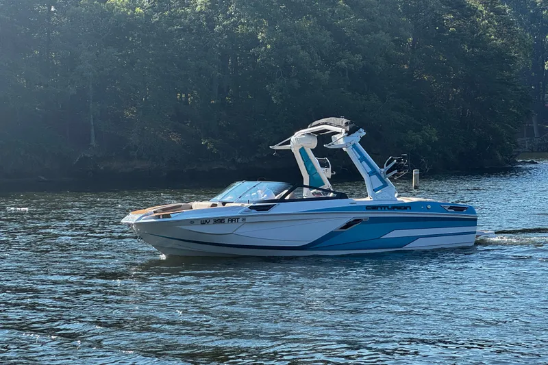 Slide: The Image of 2023 Centurion Ri230 boat cruising on a serene lake with forested background. - 2