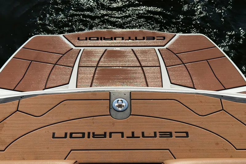 Slide: The Image of 2023 Centurion Ri230 boat deck with wood finish, featuring brand logo, on water. - 24