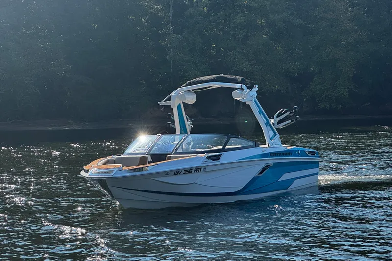 Slide: The Image of 2023 Centurion Ri230 boat cruising on a sunlit lake with forest backdrop. - 3