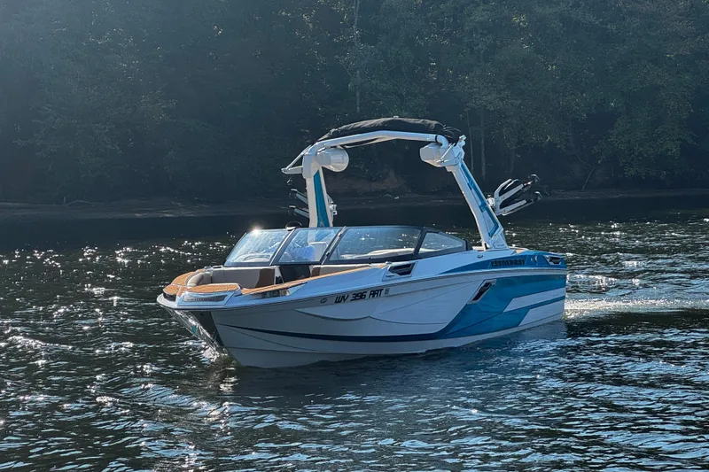 Slide: The Image of 2023 Centurion Ri230 boat cruising on a sunlit lake with forest backdrop. - 4