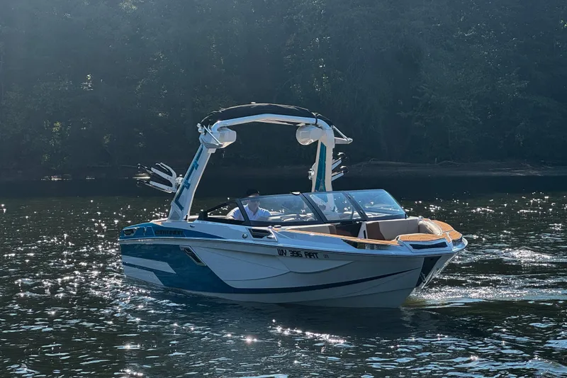 Slide: The Image of 2023 Centurion Ri230 boat on a sunlit lake with forest backdrop. - 7