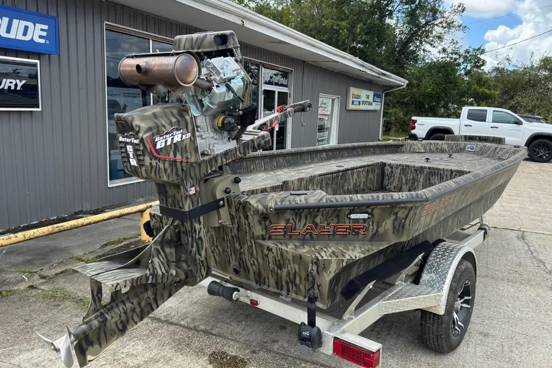 The Image of 2025 SeaArk 1752 Slayer Pro boat with camo design, parked on a trailer outside a dealership. - 1