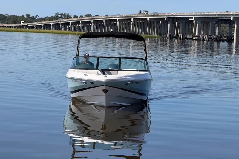 Slide: The Image of 2023 Regal 21 OBX boat cruising on calm water near a bridge. - 2