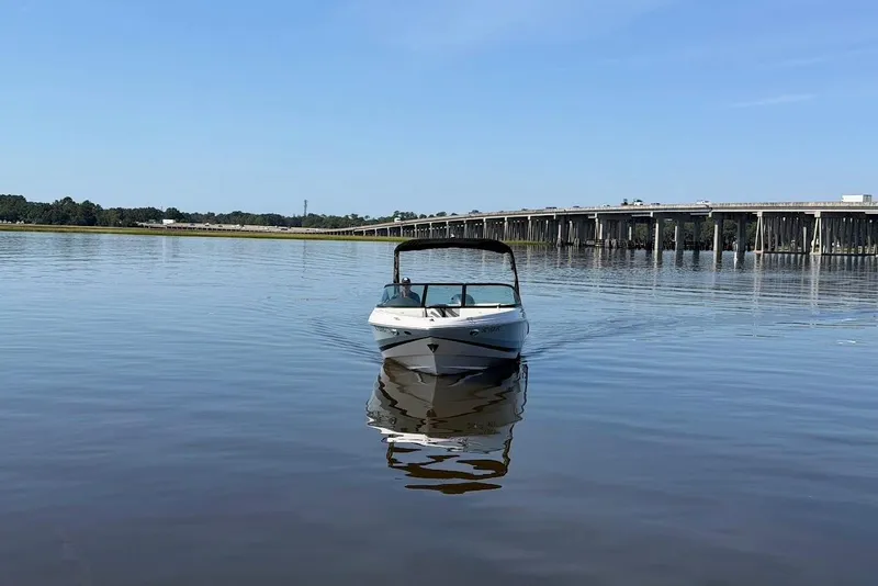 Slide: The Image of 2023 Regal 21 OBX boat cruising on calm water near a bridge under a clear blue sky. - 30