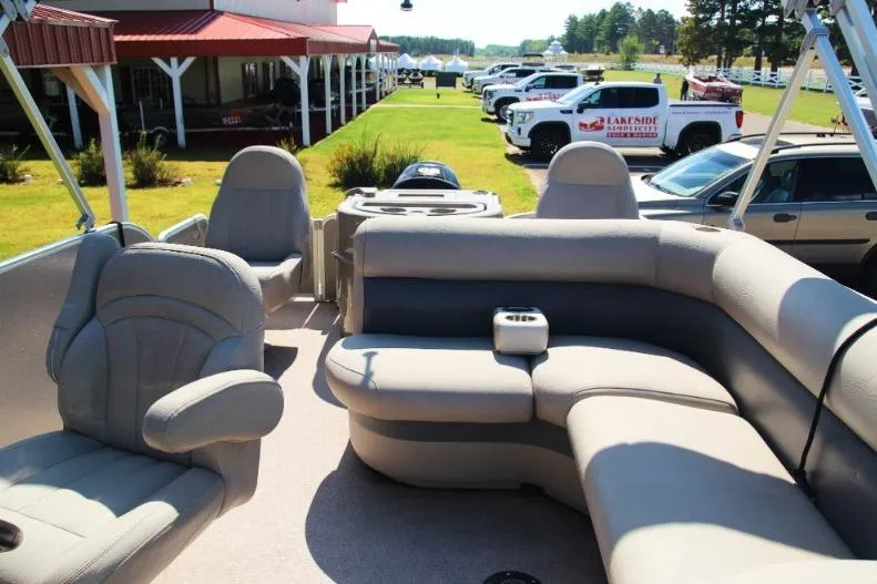 Slide: The Image of 2012 Premier 221 Gemini pontoon boat with beige seating, parked near a building and vehicles. - 10