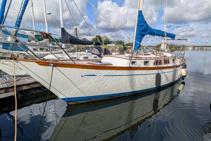 Slide: The Image of 1983 Robert Perry 41 sailboat docked, reflecting on calm water under a partly cloudy sky. - 54