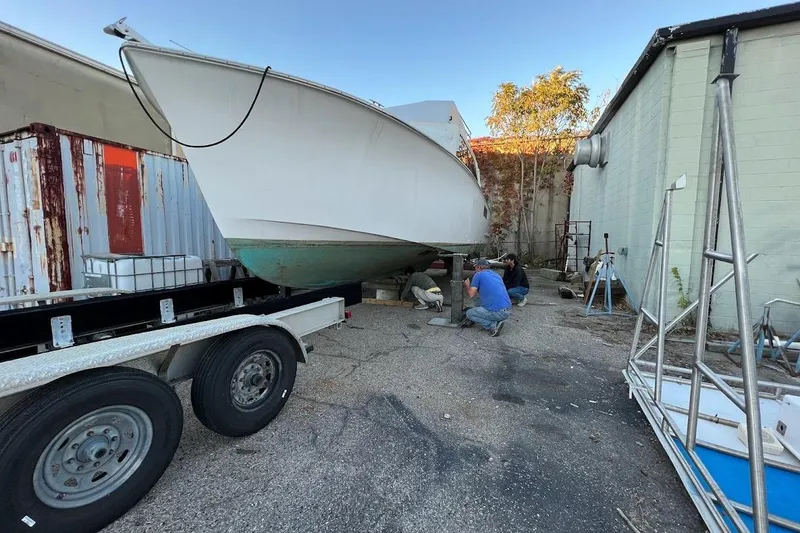 Slide: The Image of 1963 Hatteras 34 Convertible boat under maintenance in a yard with workers nearby. - 27