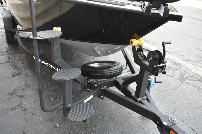 Slide: The Image of 2026 Tracker Targa V-19 WT boat trailer with steps and spare tire on asphalt. - 84