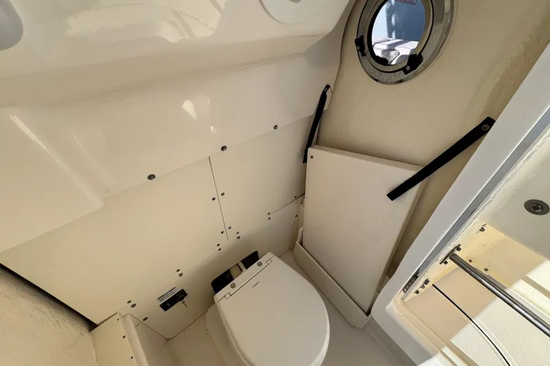 Slide: The Image of 2023 Robalo 266 Cayman boat interior with compact marine toilet and porthole. - 18