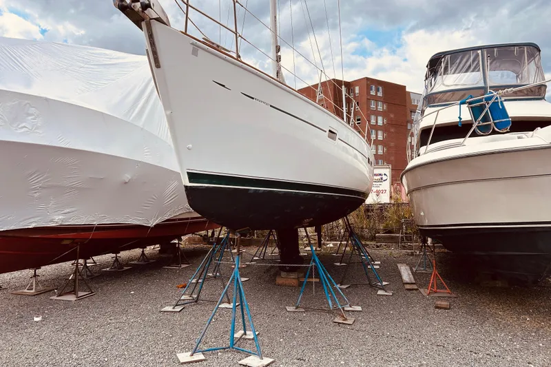 Slide: The Image of Beneteau 411 sailboat from 2001 on stands, flanked by other boats in a yard. - 34