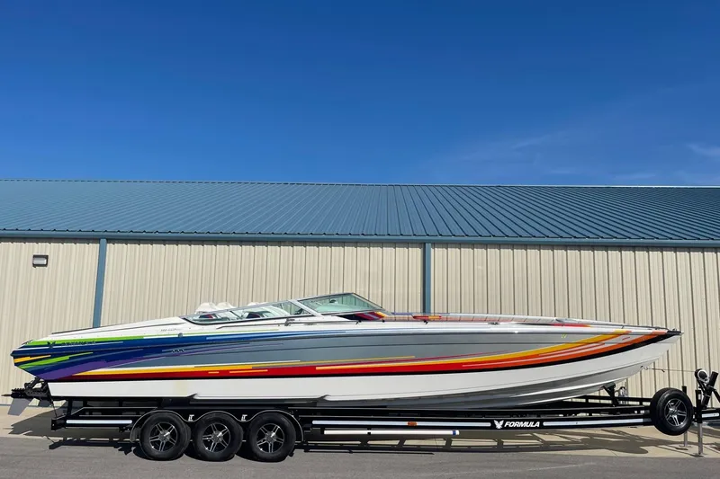 Slide: The Image of 2004 Formula 382 FASTech boat on trailer, vibrant design, parked by metal building. - 0