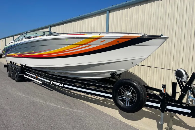 Slide: The Image of 2004 Formula 382 FASTech boat on trailer, vibrant stripes, parked by a metal building. - 4