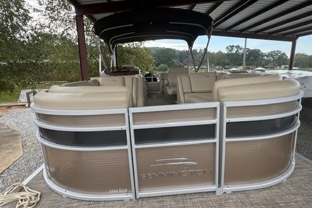 Slide: The Image of 2015 Bennington 2350 RSR pontoon boat under shelter, featuring beige seating and sleek design. - 9