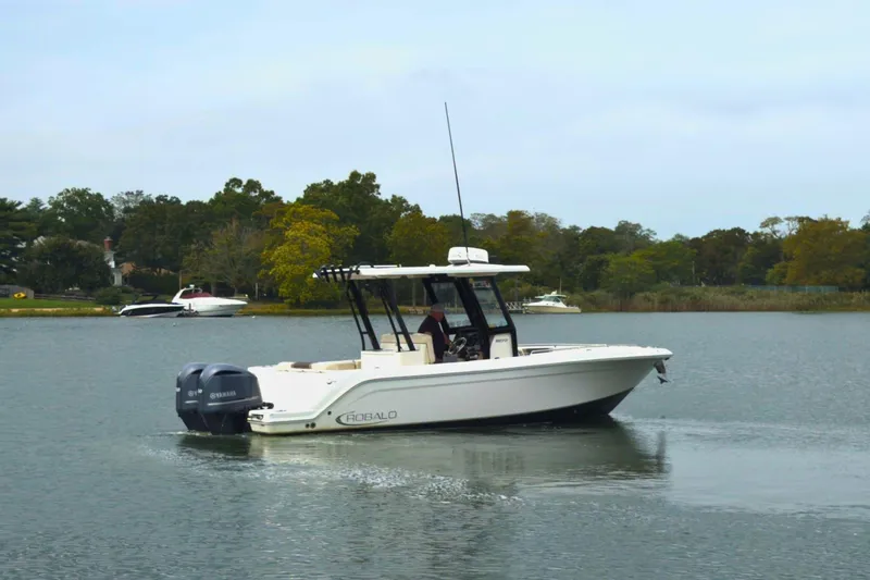 Slide: The Image of 2019 Robalo R272 Center Console boat on calm water, surrounded by trees. - 4