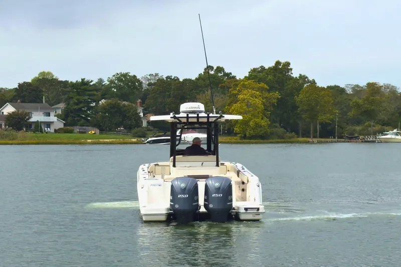 Slide: The Image of 2019 Robalo R272 Center Console boat cruising on a calm lake near a wooded shoreline. - 7