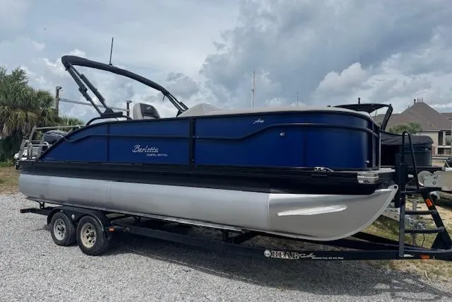 Slide: The Image of 2026 Barletta ARIA 22UC pontoon boat on trailer, parked outdoors under cloudy sky. - 2