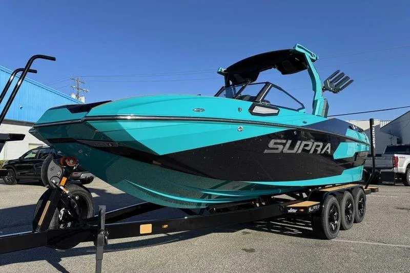 Slide: The Image of 2026 Supra SE boat in vibrant turquoise and black on a trailer, parked outdoors. - 3
