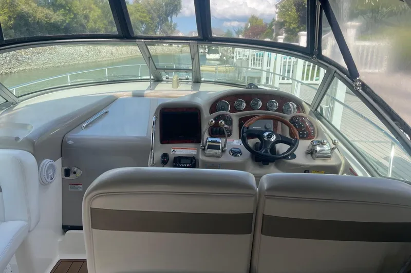 Slide: The Image of 2007 Sea Ray 320 Sundancer helm with steering wheel and control panel, docked by a river. - 11