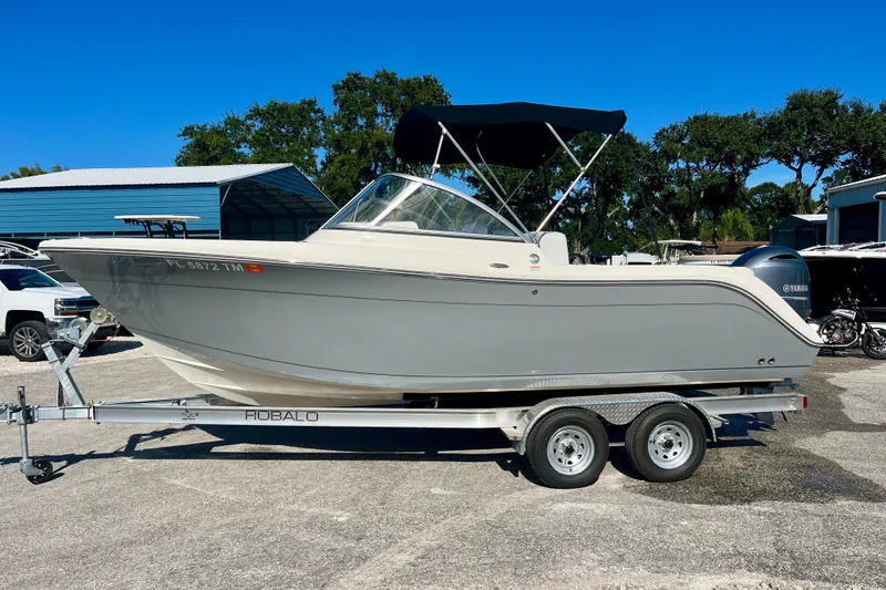 Slide: The Image of 2023 Cobia 200 DC boat on trailer, parked outdoors under clear blue sky. - 3
