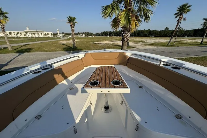 Slide: The Image of 2024 NauticStar 252 Legacy boat interior with seating and table, surrounded by palm trees. - 16